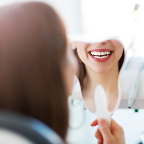 Woman with metal free dental crowns looking at her smile in mirror