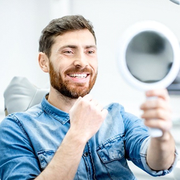 man admiring his smile in a mirror after getting dental crowns in Fort Worth, TX