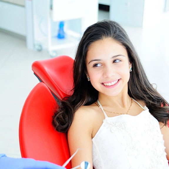 A young girl smiling while seated and waiting for a children’s dentist in Fort Worth to perform a regular checkup