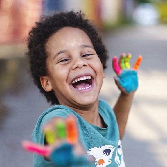 A little boy with paint on his hands showing off his healthy smile in Fort Worth