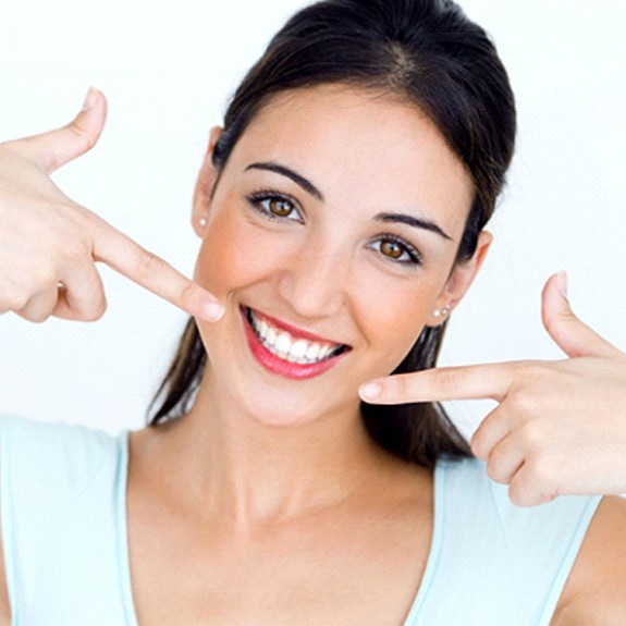 woman with dental crowns in Fort Worth pointing to her smile