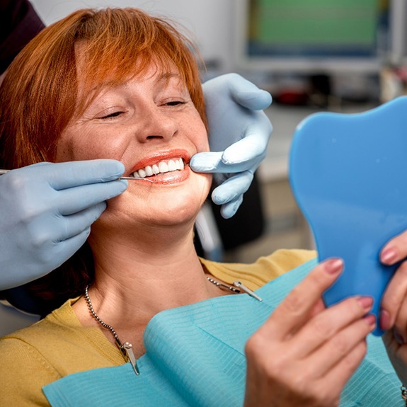 An elderly woman admiring her dentures in a hand mirror