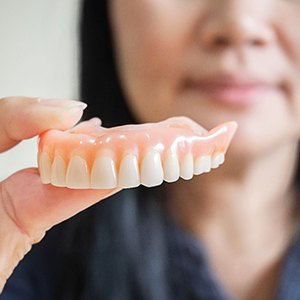 A woman holding dentures between her fingers