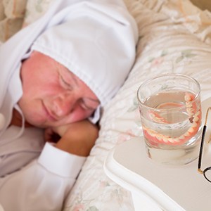 Dentures sitting in a glass next to a sleeping man