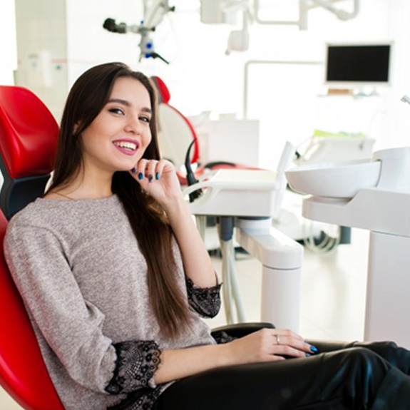 Woman smiling in patient’s chair and tapping her chin