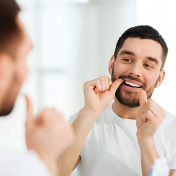 Man flossing his teeth in mirror