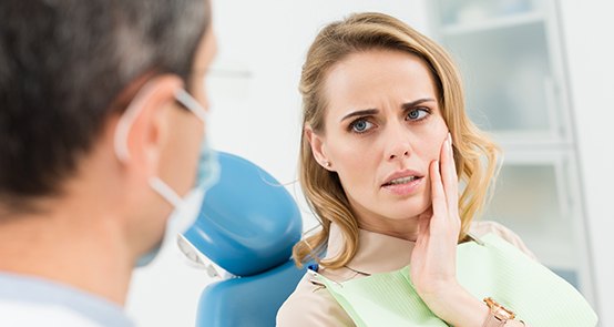 Woman in need of restorative dentistry holding cheek in pain